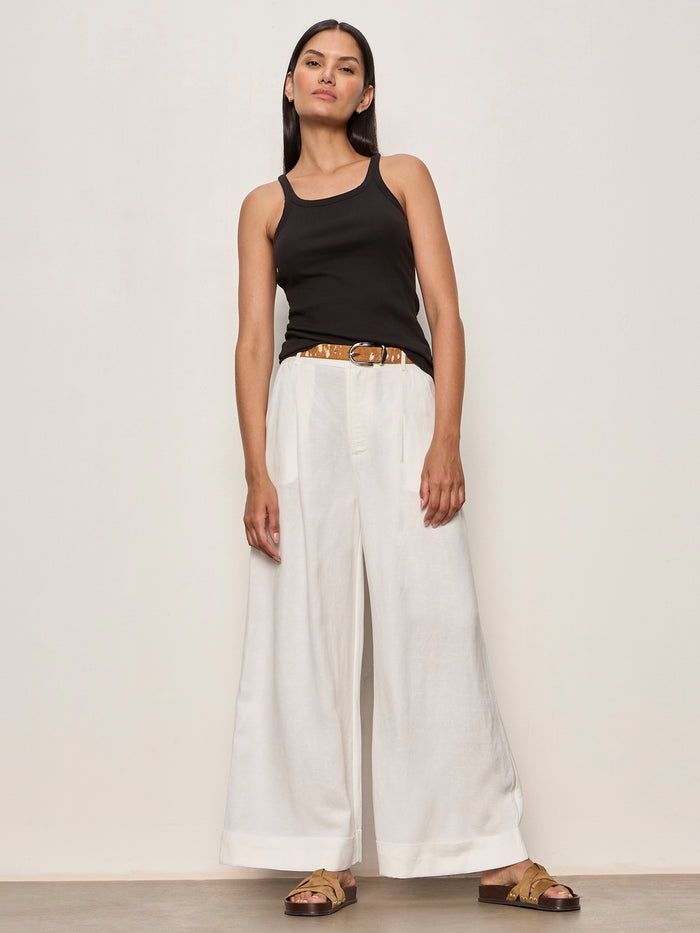 Woman wearing a black sleeveless top and white wide-leg pants against a plain background