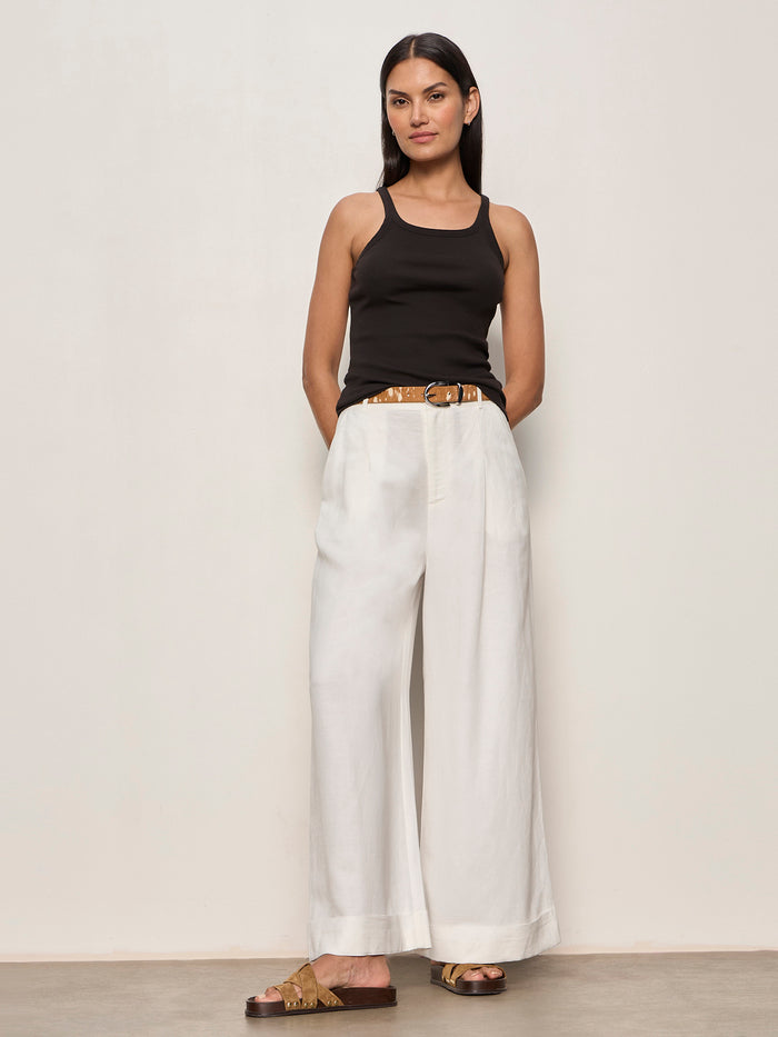 Woman wearing a black tank top and white wide-leg pants against a plain background