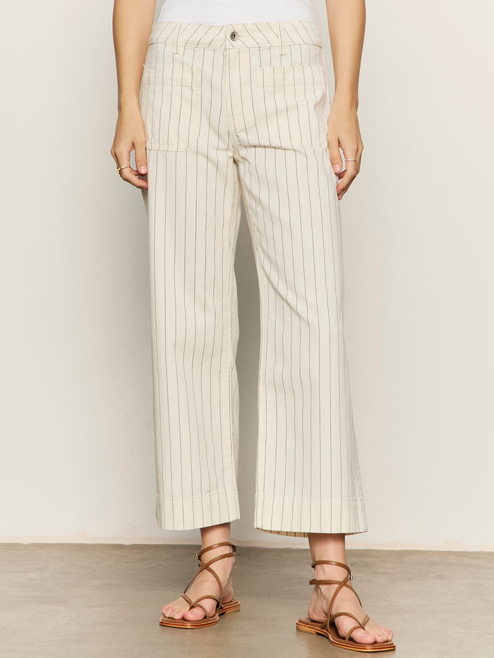 A person models the marine jean crop bleached white pinstripe by Sanctuary Clothing (petite sizing)—cream, wide-leg pants with thin vertical stripes above the ankles—paired with strappy brown sandals, upper body mostly out of frame.