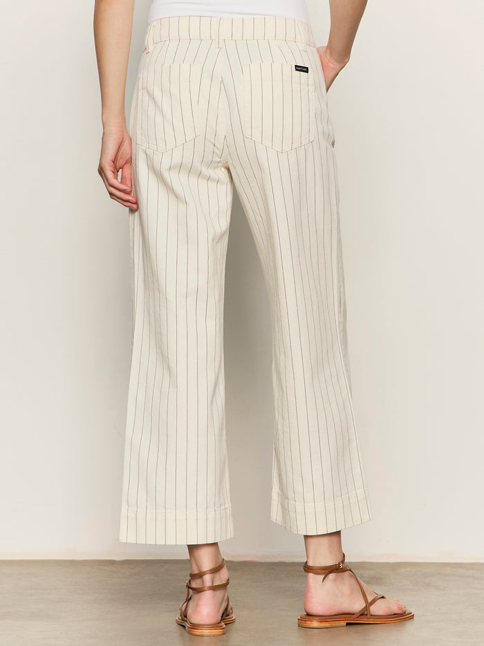 A person is seen from the back wearing Sanctuary Clothing’s Marine Jean Crop in bleached white pinstripe (petite sizing) with brown strappy sandals, against a plain background.