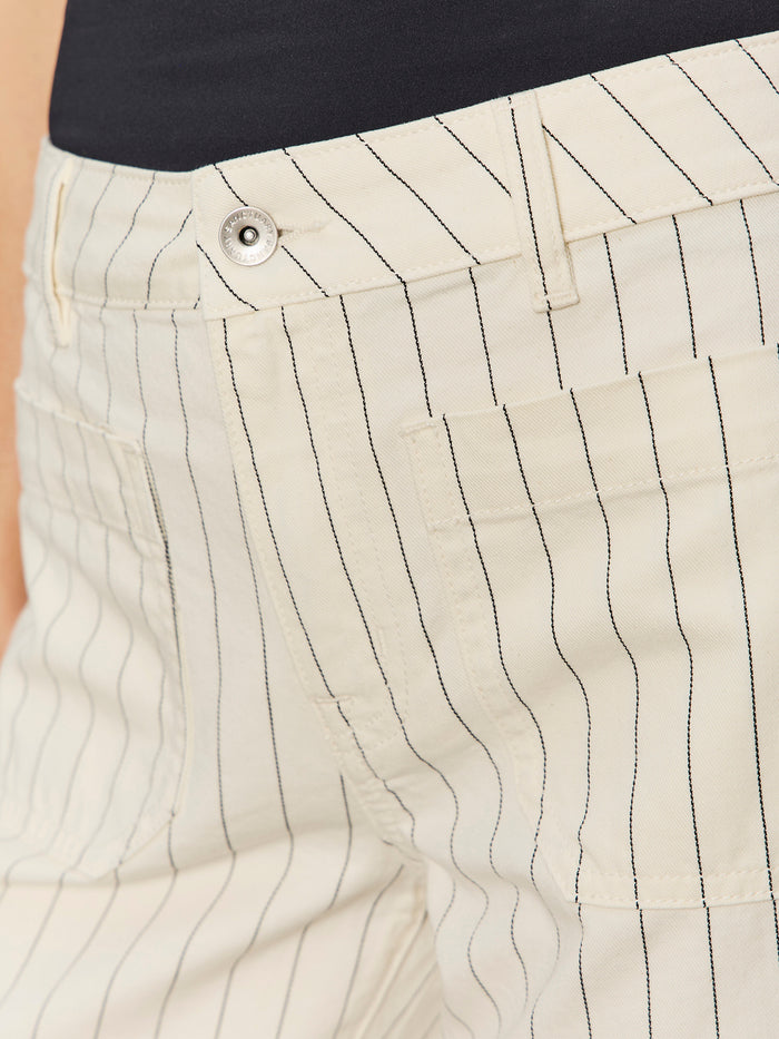 Close-up of Sanctuary Clothing's marine jean crop in bleached white pinstripe (petite), featuring a side pocket, belt loop, and silver waistband button, styled with a black top.