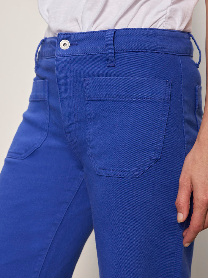 Someone wearing Sanctuary Clothing's "the marine luminous blue" jeans, paired with a white shirt. The photo highlights the waist and upper legs of the jeans, with their right arm relaxed at their side.