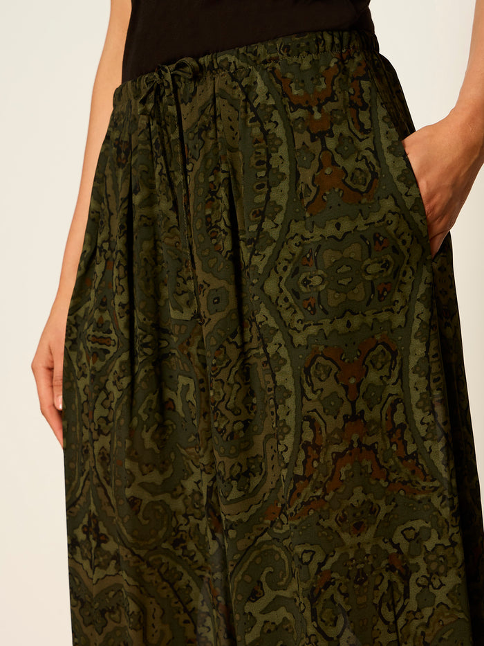 A person wears the moment volume pant in midnight moss by Sanctuary Clothing—high-waisted, dark green, paisley wide-leg pants—with one hand in a side pocket and a black top.