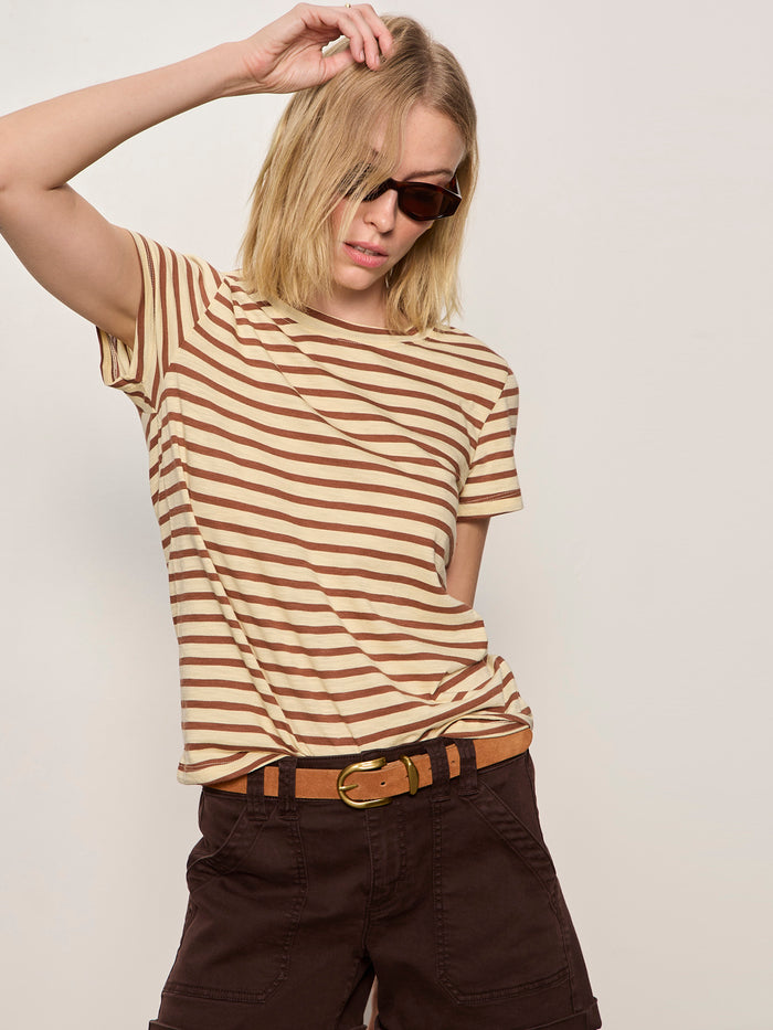A person wearing Sanctuary Clothing's the perfect tee choco banana stripe poses with sunglasses and dark brown pants, touching their head against a plain light background.