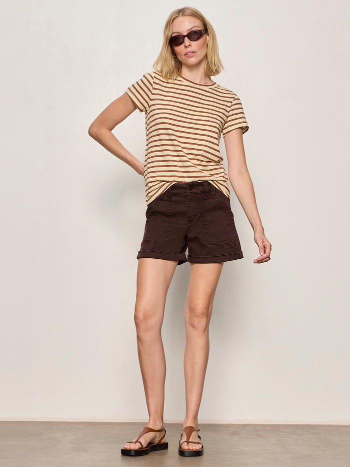 A woman models the Sanctuary Clothing "the perfect tee choco banana stripe," styled with dark brown shorts and sandals, posing against a plain light background with one hand on her hip and the other relaxed by her side.