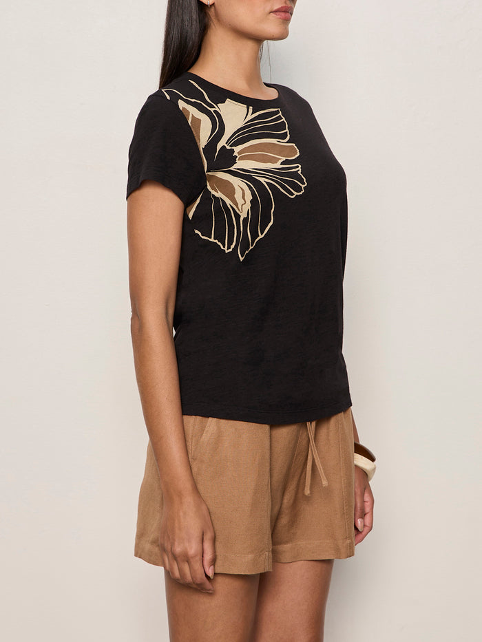 A woman stands against a plain light-colored wall wearing the Sanctuary Clothing perfect tee lotus placement and tan drawstring shorts.