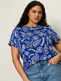 A woman with long curly hair wears the perfect tee portofino extended sizing by Sanctuary Clothing, paired with light blue jeans, standing against a plain light background.
