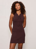 A woman with curly hair wears the tied together sweater dress in rich soil by Sanctuary Clothing, featuring a sleeveless design and lace-up neckline, standing against a plain light background with her hands behind her back.